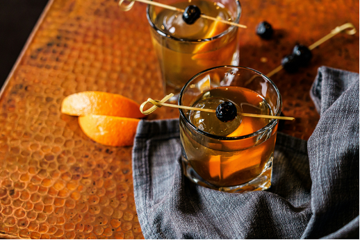 Two cocktails with skewered cherries and sliced oranges.